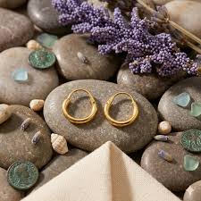 Elegant gold textured hoop earrings for women displayed on natural stones with a luxury jewelry flat lay background.